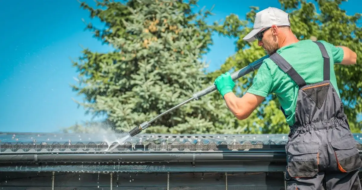 Worker pressure washing gutters on residential roof.